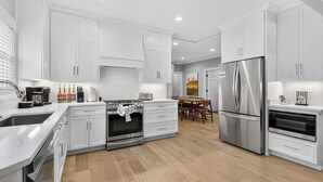A modern kitchen with white cabinetry, stainless steel appliances, and a wooden floor.
