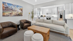 A modern living room with a large painting, leather sofas, a wooden coffee table, and a kitchen in the background.