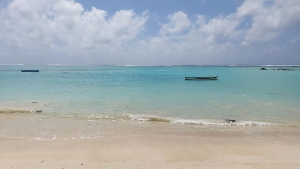 A beach with clear turquoise water, calm waves, and a few boats.