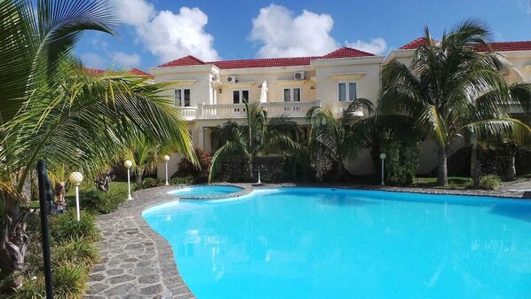 A swimming pool surrounded by palm trees and a building with a red roof.