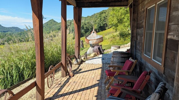 Un porche cubierto con piso de madera, sillones reclinables rojos y a rayas, un farol rústico y vistas a un paisaje verde con colinas.