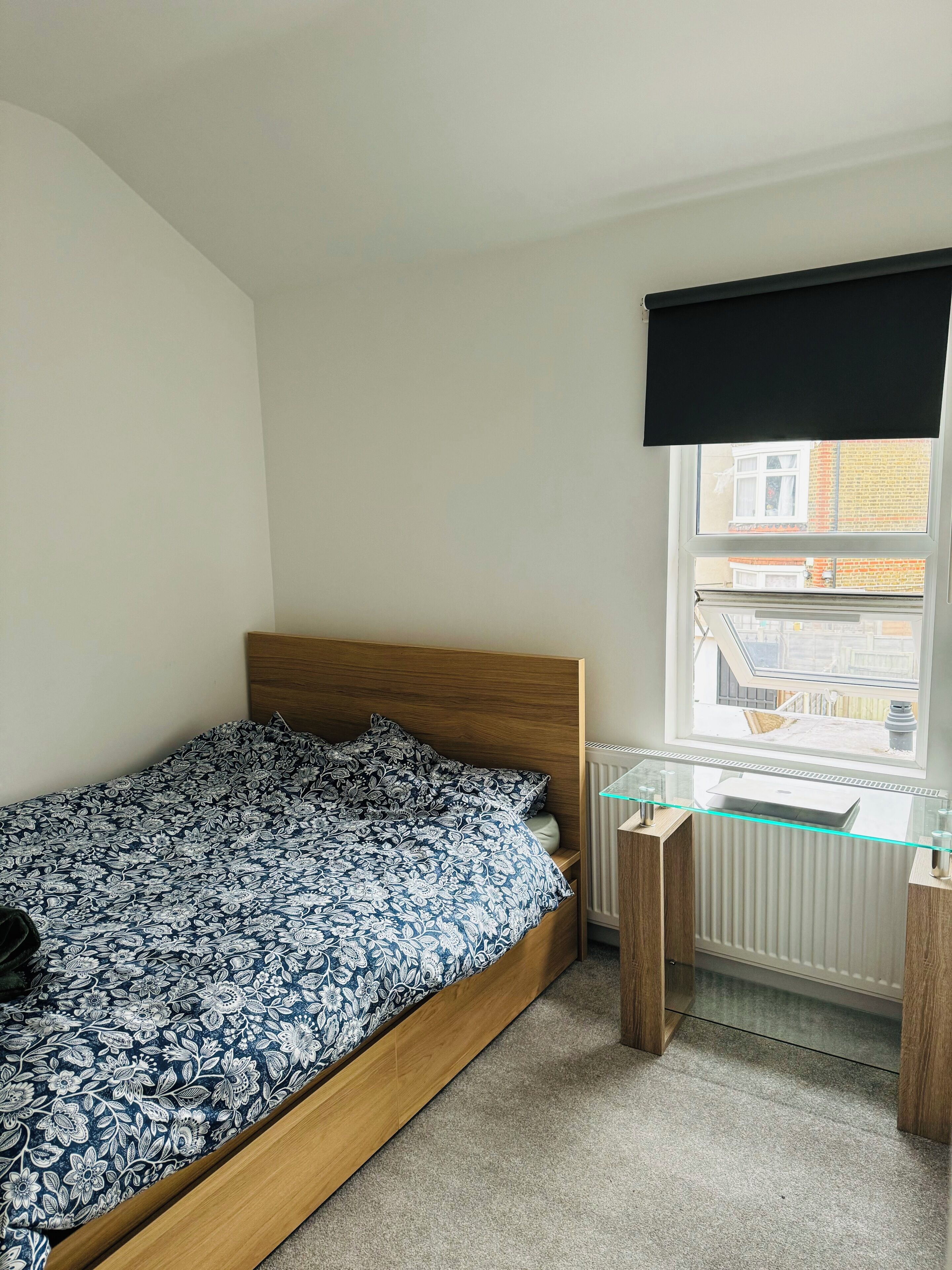 Une chambre à coucher avec un lit en bois, un bureau en verre et un radiateur.