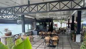 An outdoor seating area with tables and chairs, surrounded by large green plants.