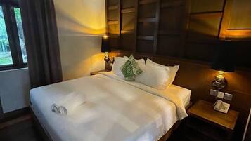 A neatly made bed with a white comforter and pillows, a bedside table with a lamp, and a window with curtains.