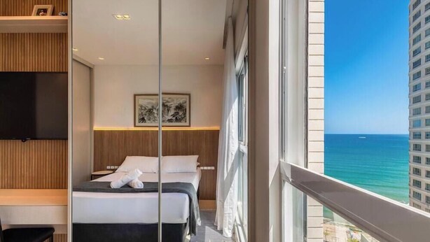 A hotel room with a bed, a TV, a framed artwork, and a view of the ocean. - 3-bedroom Apartment 170m From the Beach Gua1902 (Balneário Camboriú)