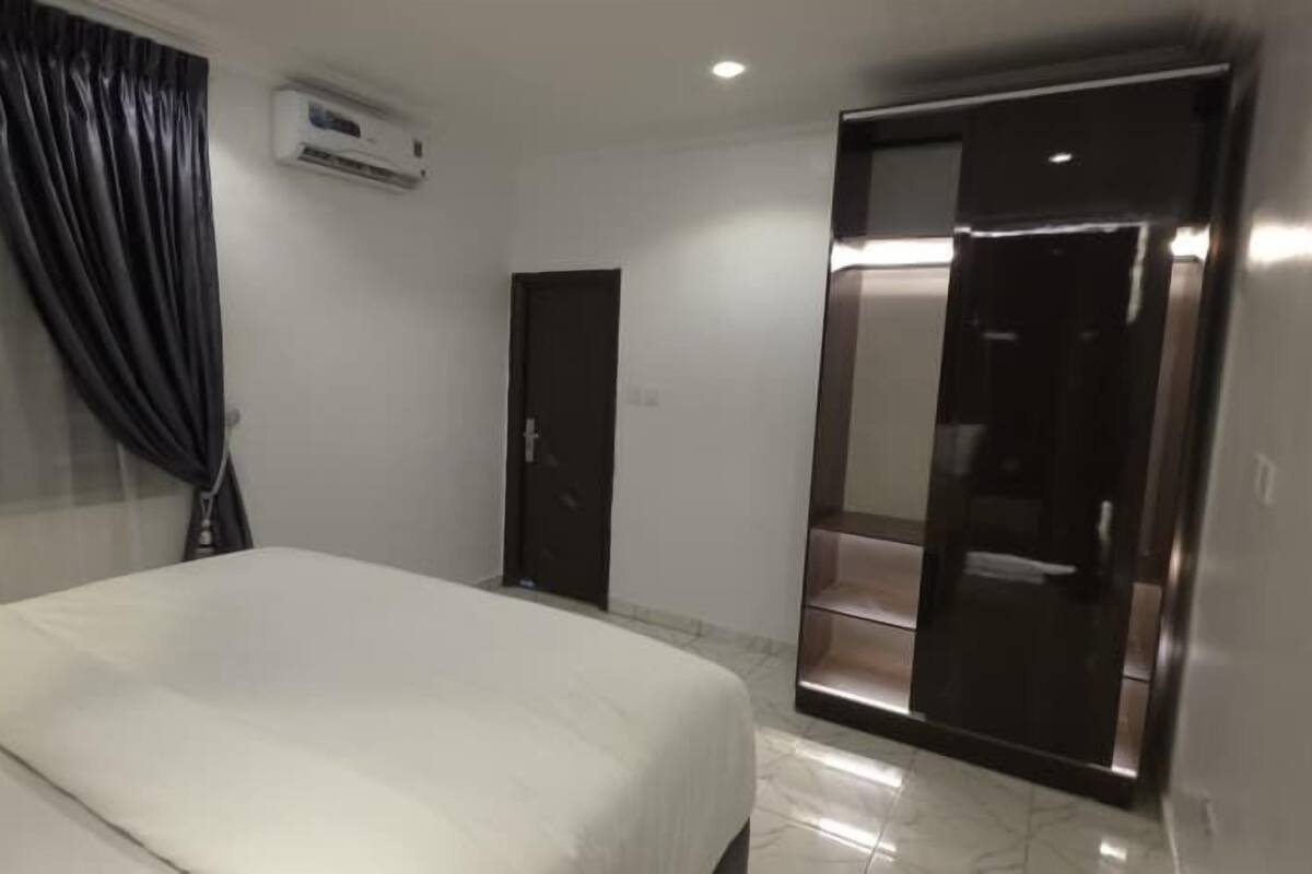 A hotel room with a bed, a wardrobe, a door, and an air conditioning unit.