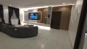 Un salon moderne avec un canapé d’angle aux lignes courbes, un téléviseur à écran plat fixé au mur et un mur décoratif en panneaux de bois.