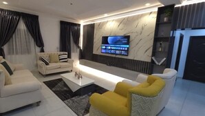 Un salon moderne avec un téléviseur à écran plat fixé au mur, un canapé, une table basse et un fauteuil jaune.