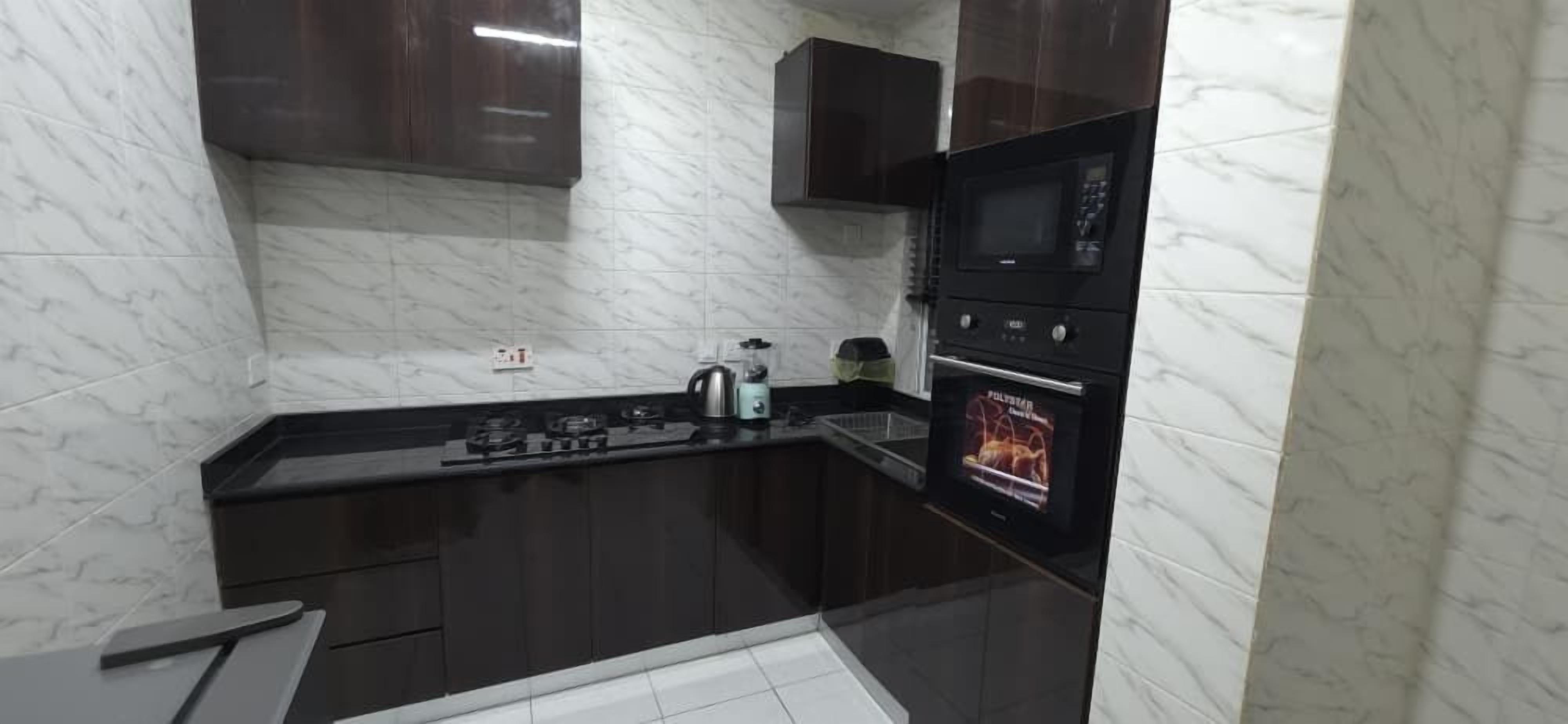 A compact kitchen with dark cabinets, a black countertop, a built-in microwave, and a stove.