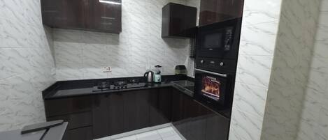 A compact kitchen with dark cabinets, a black countertop, a built-in microwave, and a stove.