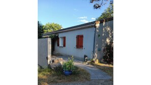 A building with a white exterior and red shutters, a gravel path, and a blue planter with green plants. - Spacious "la falaise" house in the beautiful listed village of Balazuc (Balazuc)