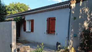 A building with a white exterior and red shutters, a gravel path, and a blue planter with green plants. - Spacious "la falaise" house in the beautiful listed village of Balazuc (Balazuc)