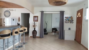 A spacious living area with a kitchen, a dining area with bar stools, a large woven light fixture, and a door with a bulletin board. - Spacious "la falaise" house in the beautiful listed village of Balazuc (Balazuc)