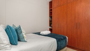 Une chambre à coucher avec un lit, des oreillers, une armoire en bois et une petite étagère avec des livres.
