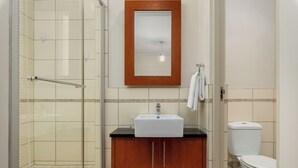 Une salle de bain avec une douche à parois de verre, un meuble en bois avec un lavabo et des toilettes.