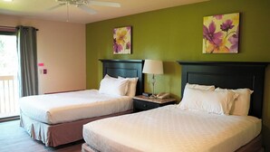 A hotel room with two beds, a ceiling fan, a window with curtains, and floral artwork on the walls.