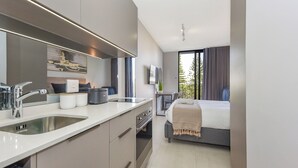 Habitació d'hotel moderna amb zona de cuina, un llit, televisió i un balcó amb cortines.
