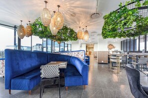 Un espace de détente moderne avec un canapé bleu, des lustres en cristal suspendus et une installation décorative au plafond composée de feuilles vertes.