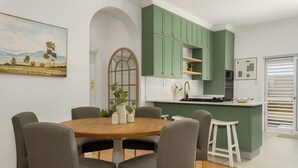 Une cuisine moderne avec des meubles de couleur verte, une table à manger en bois avec six chaises et une grande fenêtre donnant sur un paysage arboré.