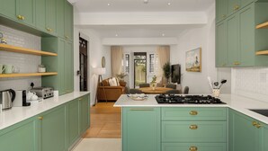 Une cuisine moderne avec des meubles verts, des plans de travail blancs et un îlot central. On aperçoit à l’arrière-plan un coin repas avec une table et des chaises.