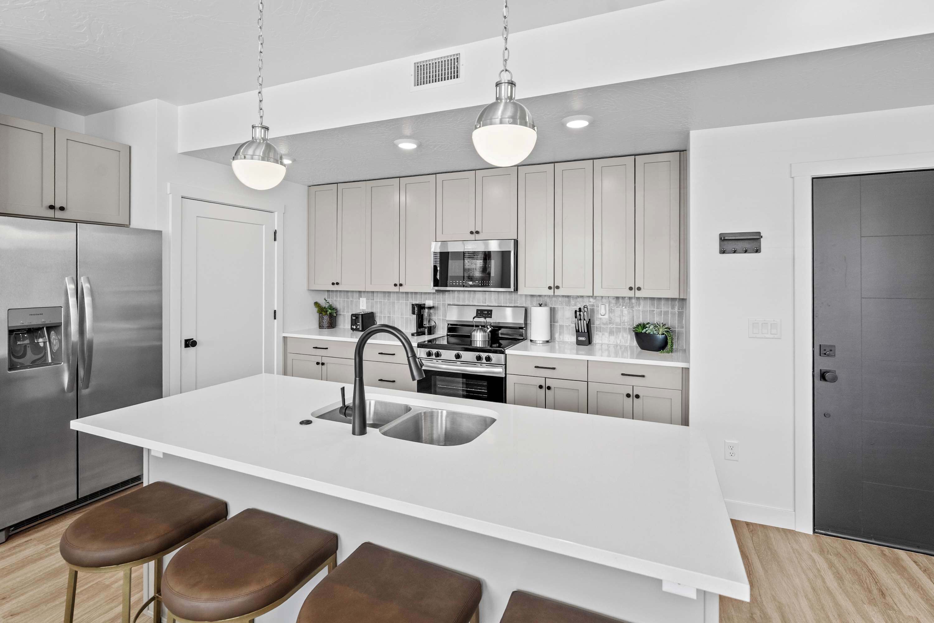 A modern kitchen with stainless steel appliances, a white island with bar stools, and pendant lighting.