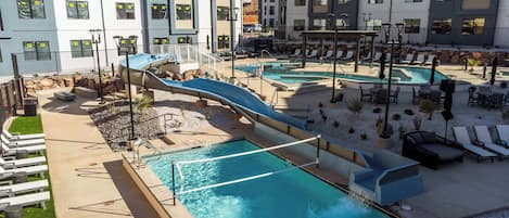 Ein modernes Hotel mit mehreren Schwimmbecken, einer Wasserrutsche und Sitzbereichen im Freien.