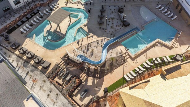 Ett flygbildsfoto av ett hotell med flera pooler, inklusive en vattenrutschkana, loungeområden och utomhusmöbler.