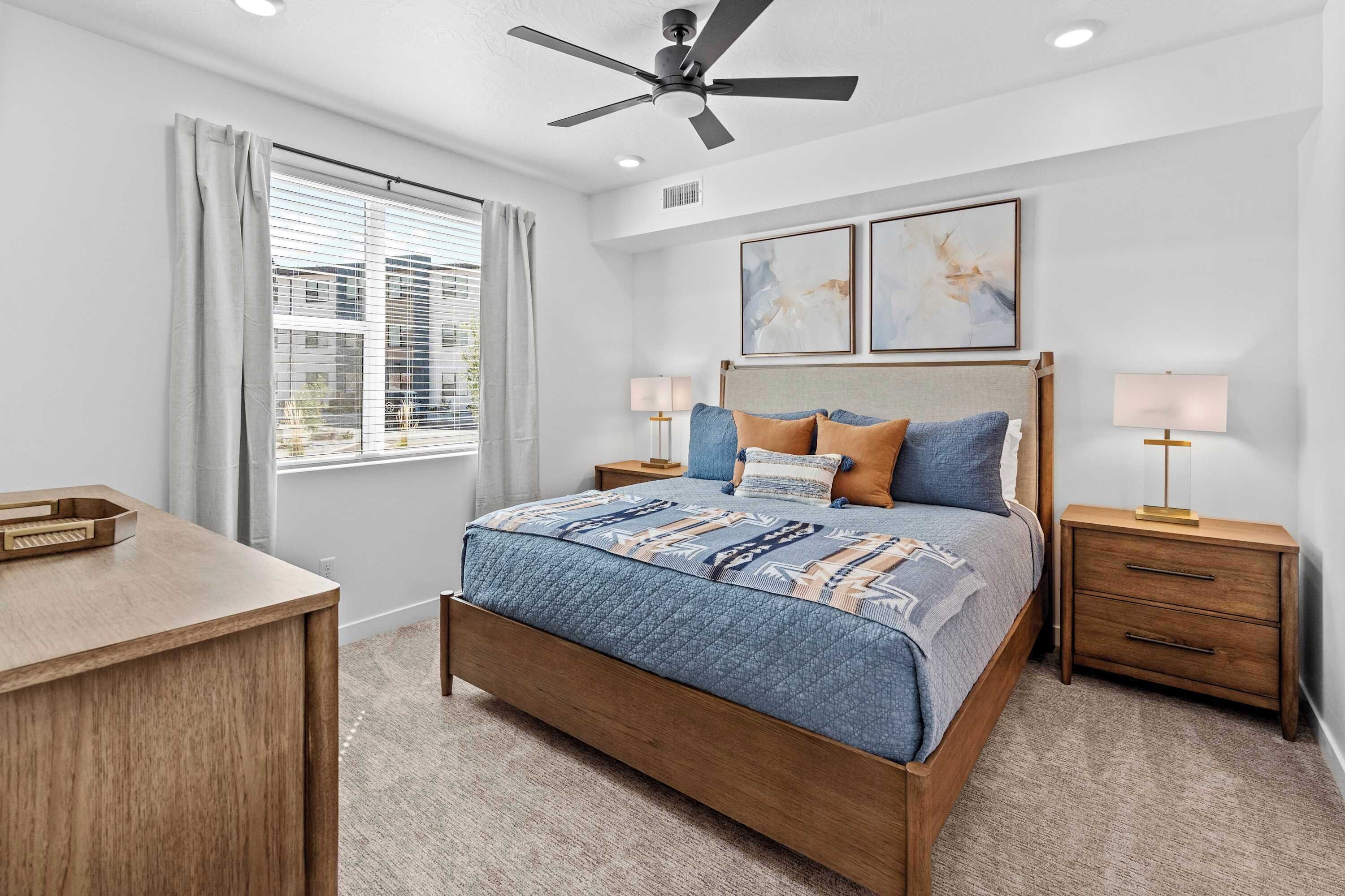 A bedroom with a bed, two bedside tables, a ceiling fan, and a window with blinds.