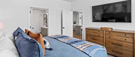 A bedroom with a bed, a dresser, a ceiling fan, and a TV on the wall.