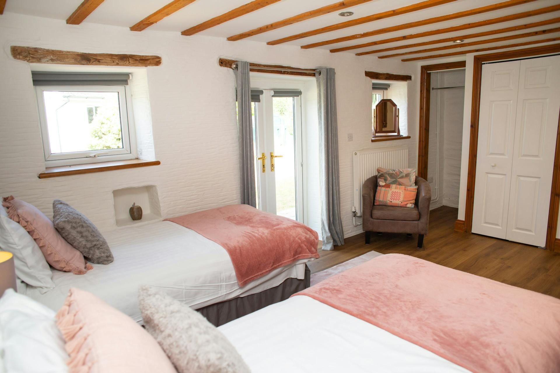A bedroom with two beds, wooden beams, a window, a radiator, and a door.