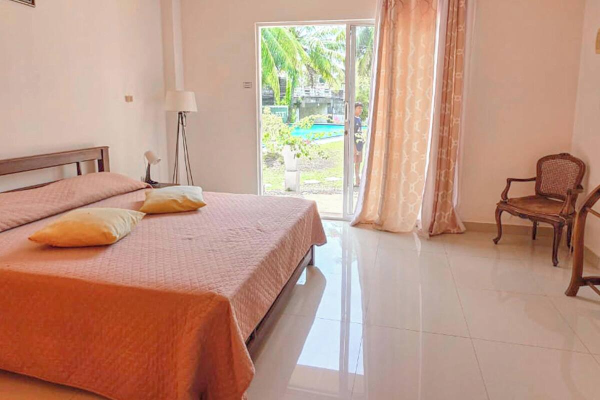 A hotel room with a bed, a chair, a lamp, and a view of a pool.