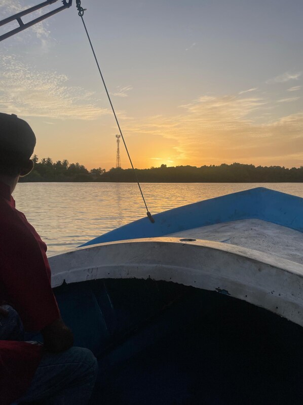 A boat with a person on board, facing a sunset over a body of water. - Lake View Resort (Pamunugama)