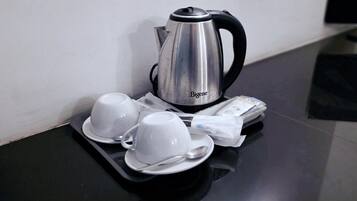 Una bandeja con un hervidor plateado, dos tazas blancas, una cuchara y un paquete de pañuelos sobre una mesa negra.