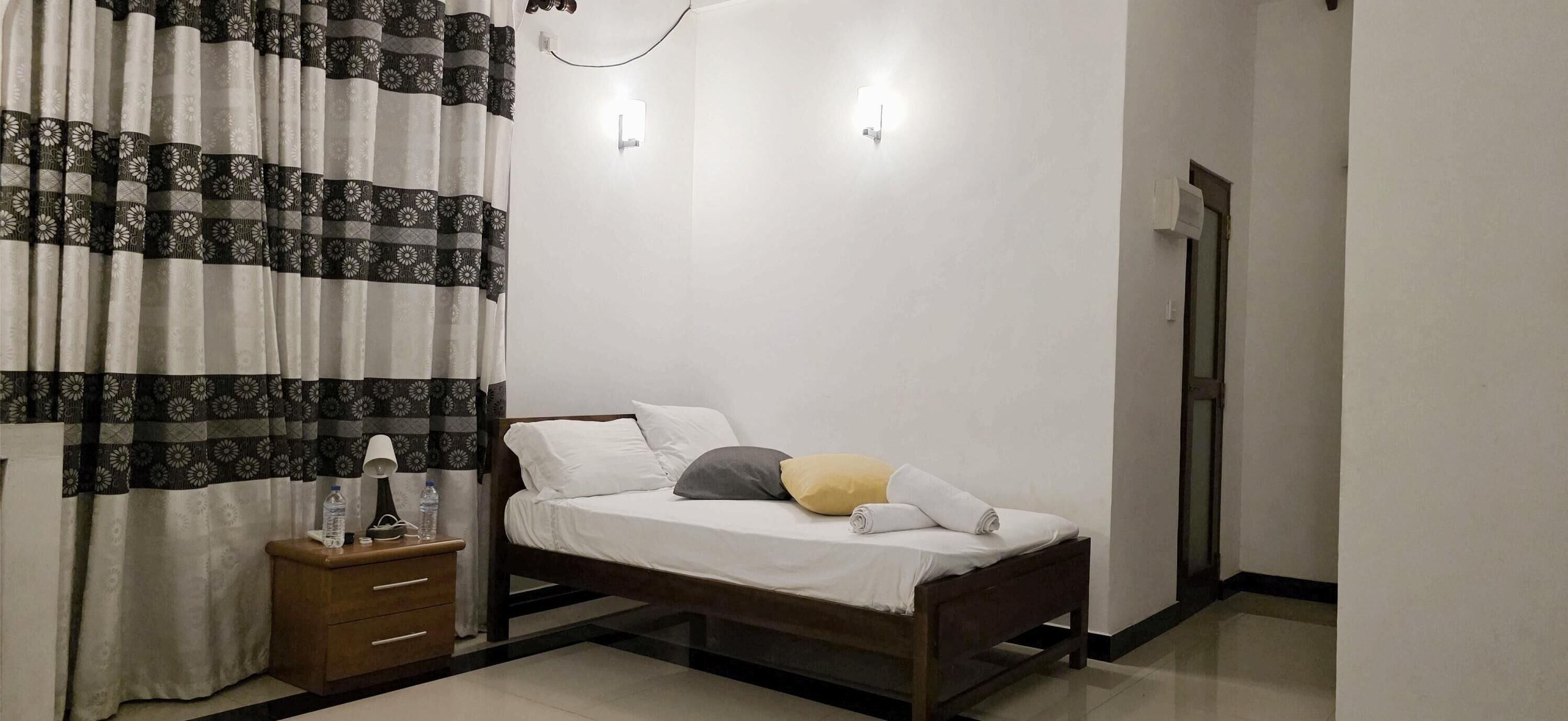 A bedroom with a bed, bedside table, curtains, and a wall-mounted light fixture.