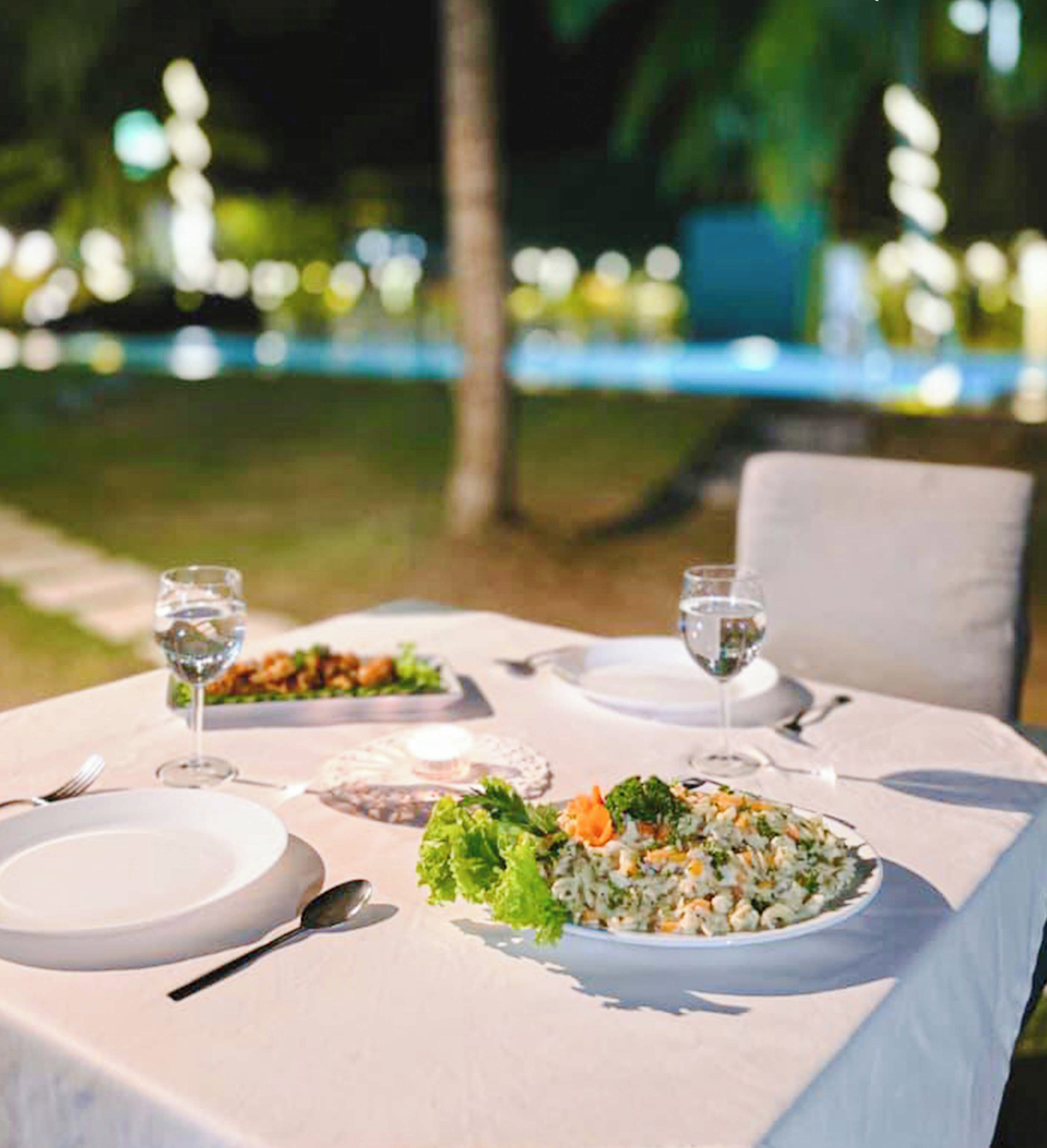 An outdoor dining setup with a white tablecloth, two plates of food, and two glasses of water.