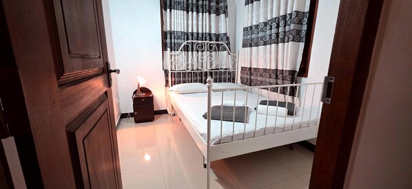 Een slaapkamer met een bed met een wit metalen frame, een nachtkastje met een lamp en behang met een patroon.