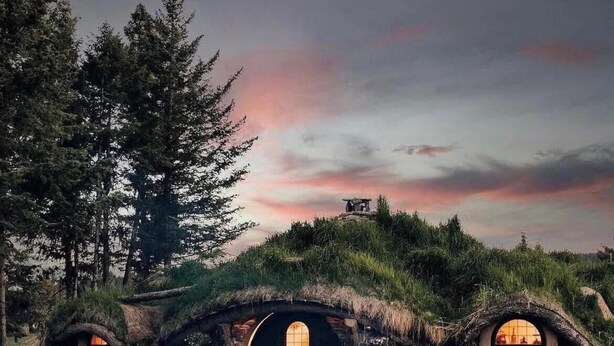 A fantasy-style house with circular windows and thatched roofs, surrounded by greenery and a twilight sky.