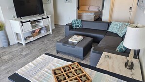 A modern living room with a flat-screen TV, grey sofa, and a coffee table with a decorative wooden tray.