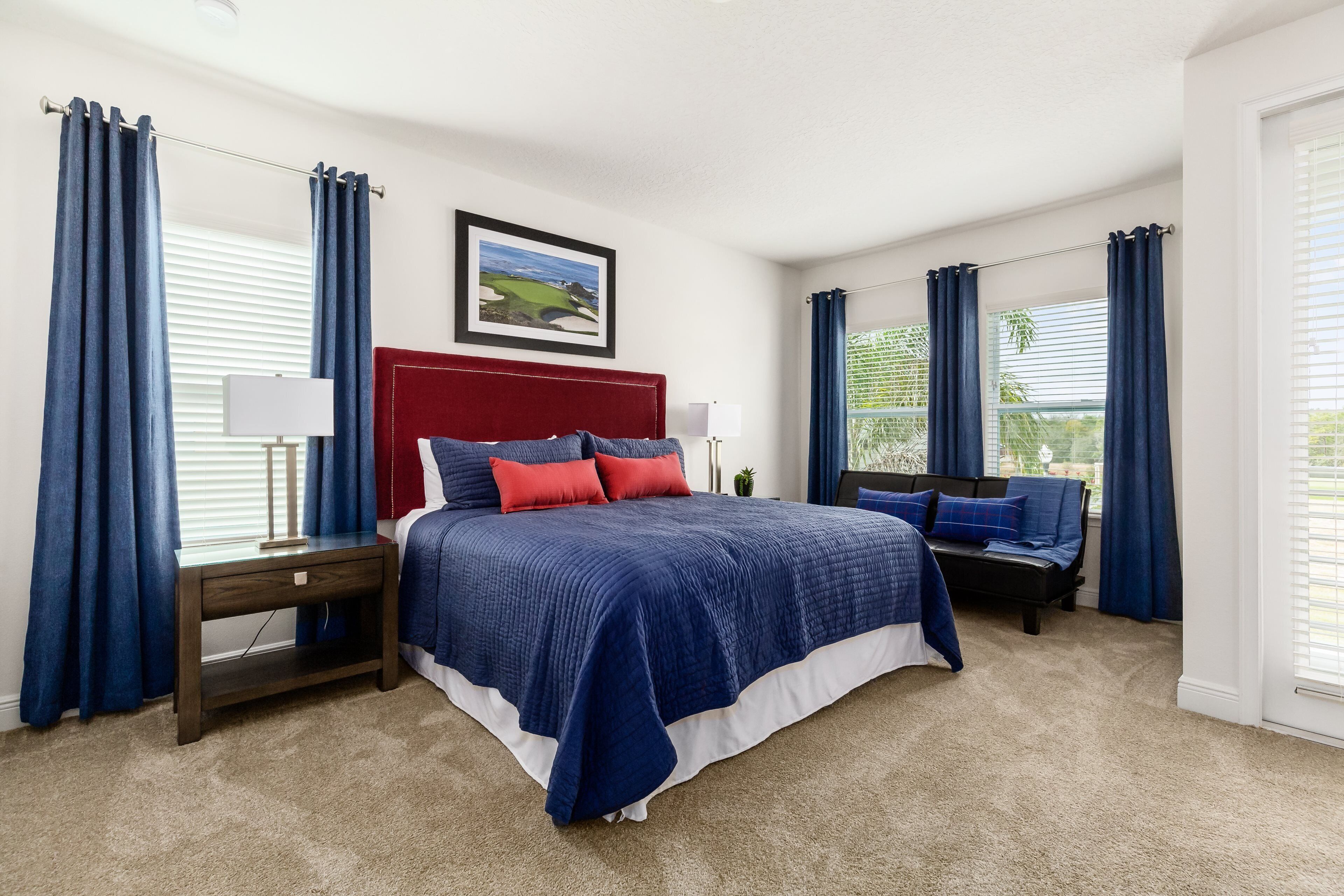 A bedroom with a large bed, a red headboard, and blue curtains.
