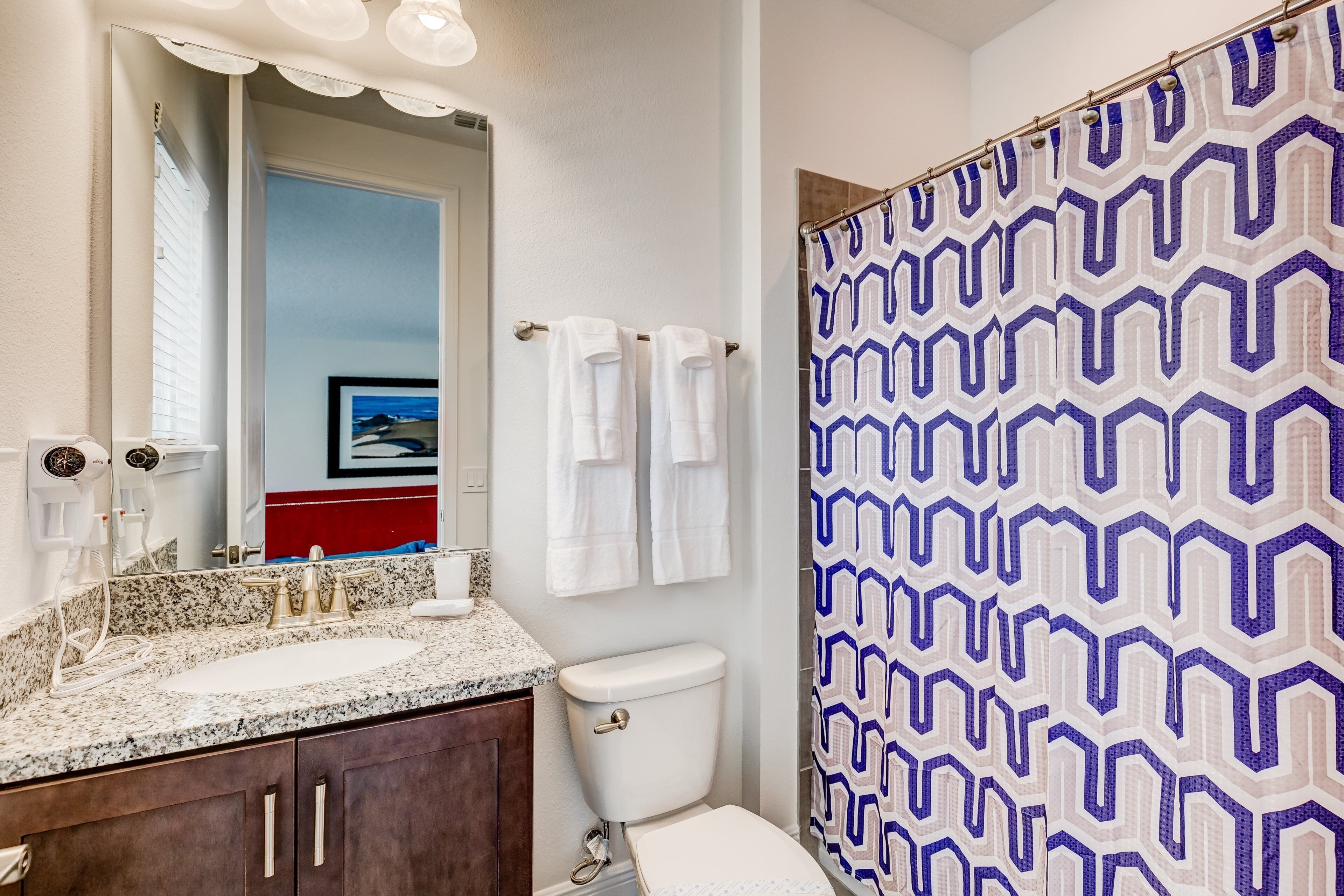 Une salle de bain avec un lavabo sur un plan de toilette en granit, des toilettes et un rideau de douche à motifs géométriques.