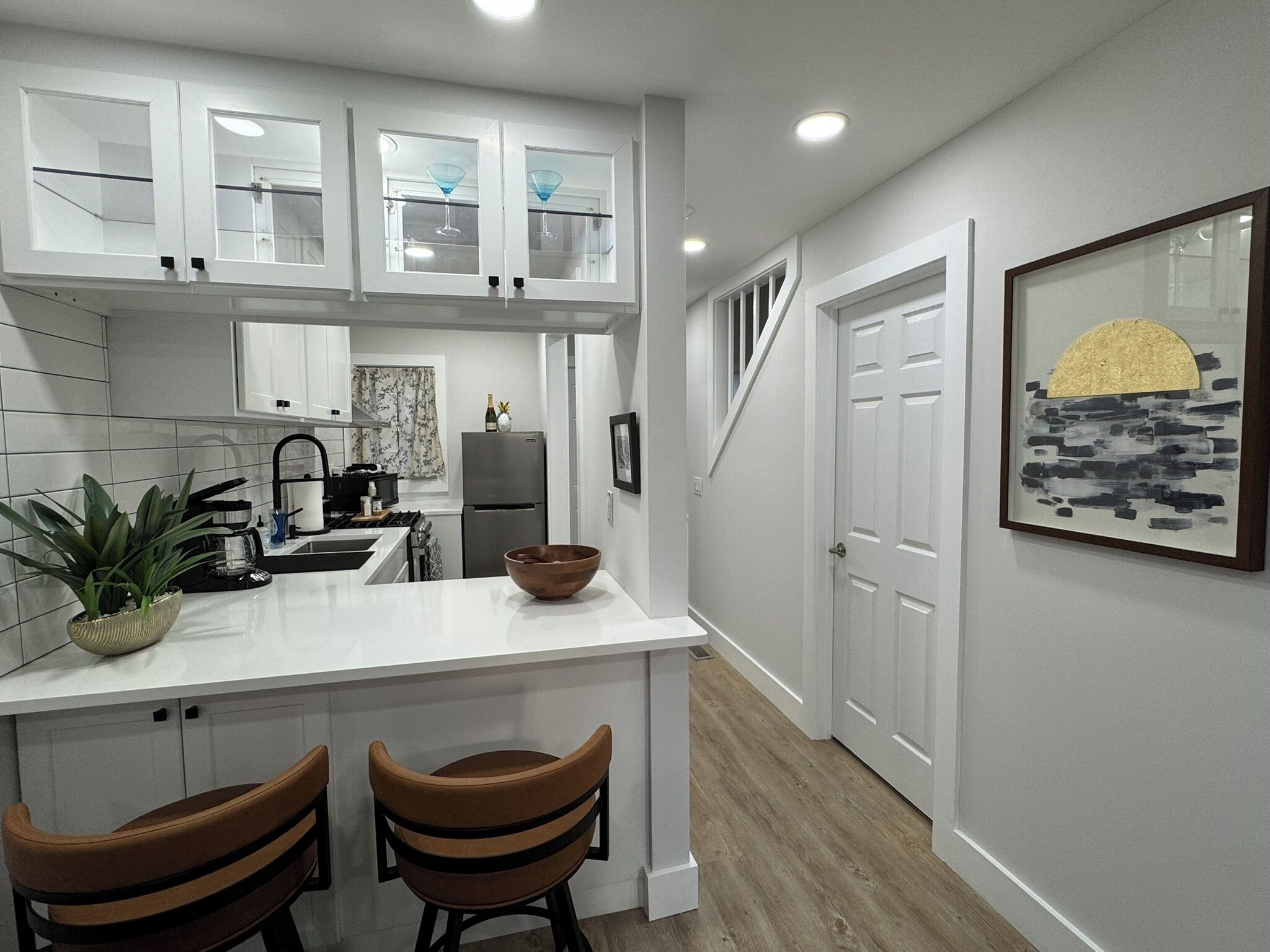 A modern kitchen with white cabinetry, a central island with two bar stools, a refrigerator, and a sink.