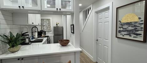 A modern kitchen with white cabinetry, a central island with two bar stools, a refrigerator, and a sink.