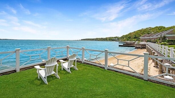 A waterfront view with a deck, white chairs, and a sandy beach area. - Heart of the Hamptons, Waterfront with Pool!  1 Bed/1 Bath Townhome (Hampton Bays)