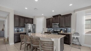 A modern kitchen with dark wood cabinets, stainless steel appliances, and a granite countertop island with four chairs. - Last Minute Disney! Private Pool, Hot Tub, Game Room & Themed Bedrooms. Book Now! #37046 (Orlando)