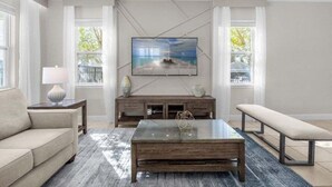 A modern living room with a large flat-screen TV mounted on the wall, a glass coffee table, a bench, and a sofa. - Last Minute Disney! Private Pool, Hot Tub, Game Room & Themed Bedrooms. Book Now! #37046 (Orlando)