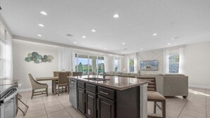 A modern kitchen with a central island, dining area with chairs, and a large window offering a view. - Last Minute Disney! Private Pool, Hot Tub, Game Room & Themed Bedrooms. Book Now! #37046 (Orlando)