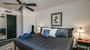 Une chambre à coucher comprenant un lit, un ventilateur de plafond, des œuvres d’art et une table de chevet avec une lampe.