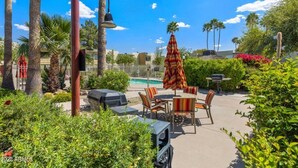 Un espace extérieur aménagé avec une terrasse, une piscine, des sièges et un grand parasol.
