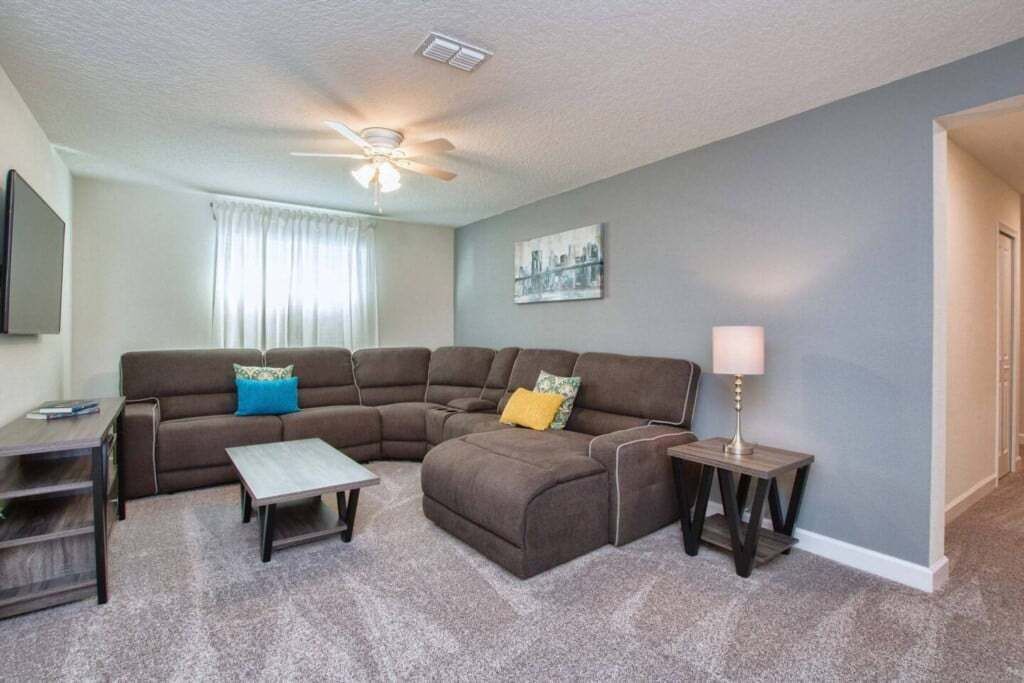 A living room with a sectional sofa, a coffee table, a lamp, and a ceiling fan.