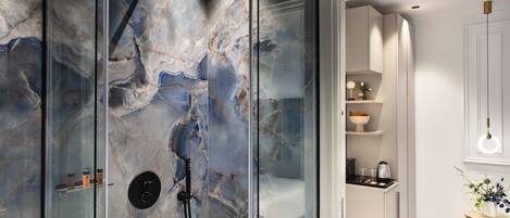 Un baño moderno con cabina de ducha de vidrio, paredes de mármol y una pequeña zona de kitchenette.